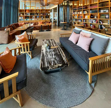 Lounge mit Holzsofas, bunten Kissen und rundem Teppich vor Bücherregalen