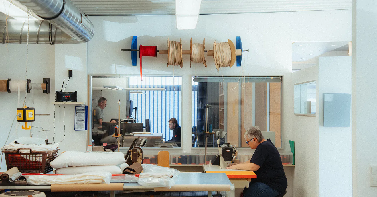 Werkstatt von Albersmeyer mit Zuschnitttischen, Garnrollen und Mitarbeitern bei der Arbeit