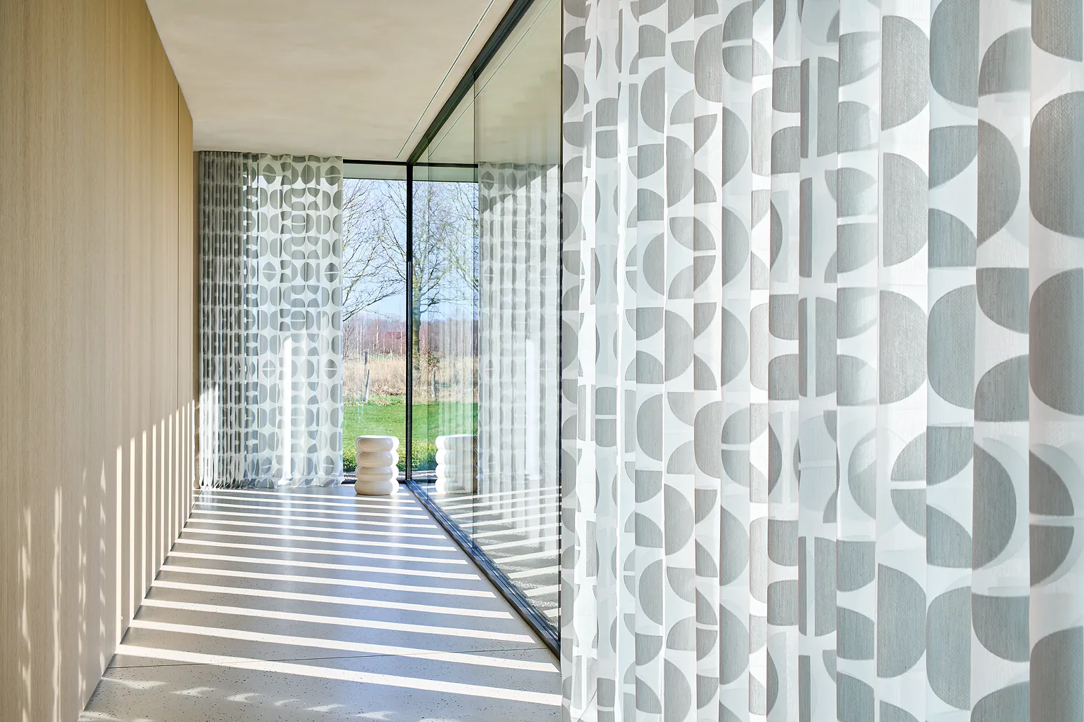 Transparente Gardinen mit grafischem Muster in einem Flur mit Glasfront