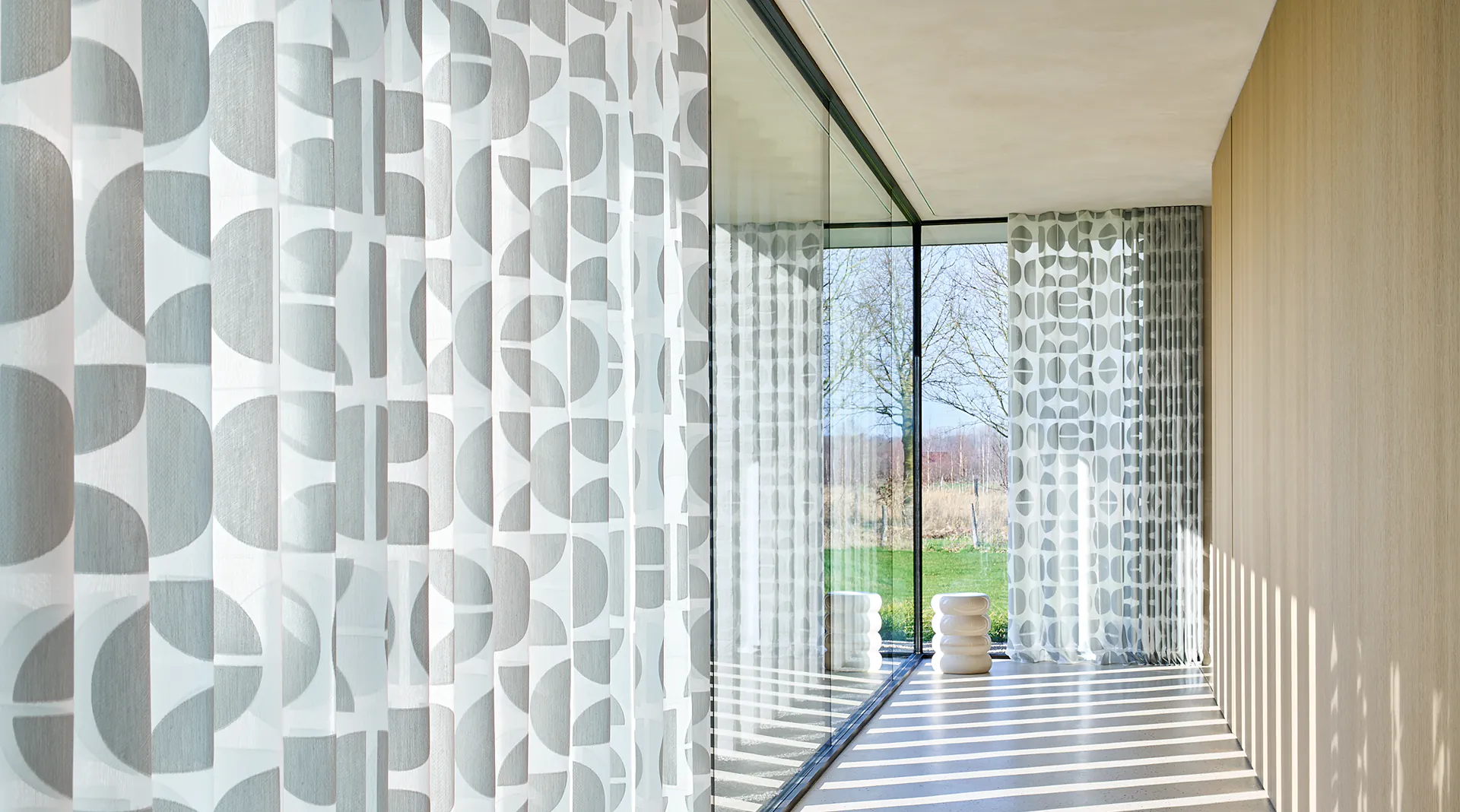 Transparente Gardinen mit grafischem Muster an einer bodentiefen Glasfront