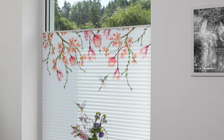 Plissee mit Blüten- und Kolibri-Motiv als Sonnenschutz am Fenster