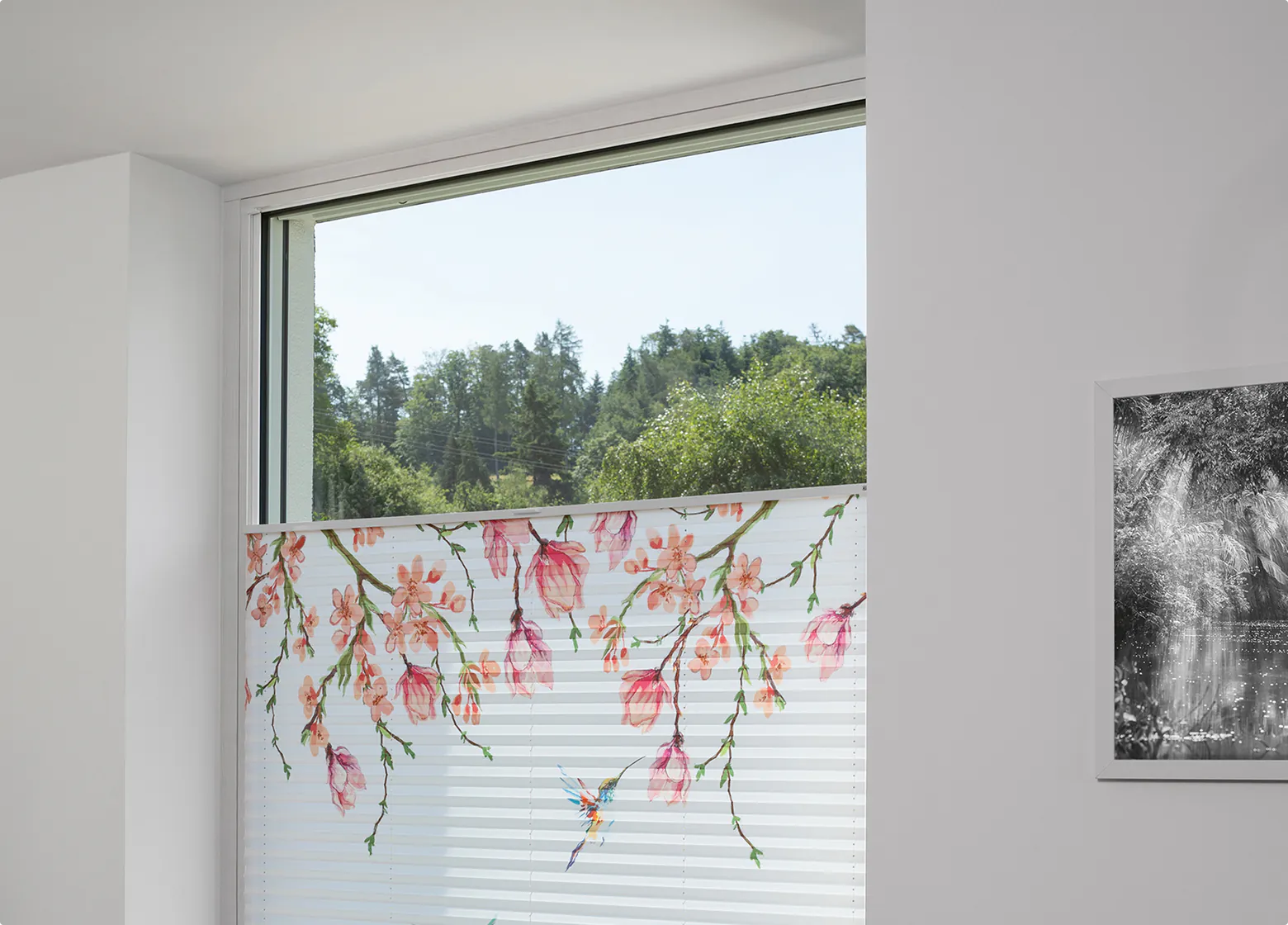 Weißes Plissee mit Blütenmotiv am Fenster eines hellen Wohnraums