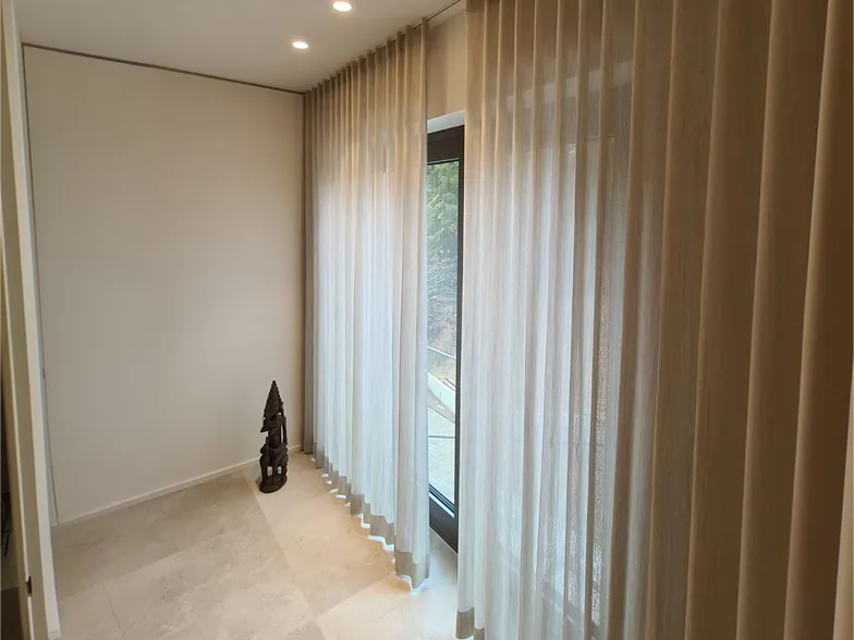 Wellenvorhänge in Sand und Weiß an der Fensterfront eines Wohnbereichs