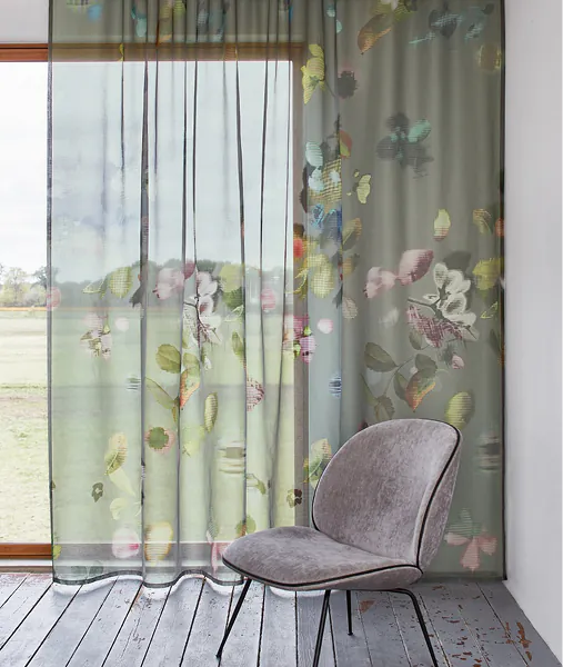 Transparenter Vorhang mit Blumendruck an einer Fensterfront, davor ein Sessel